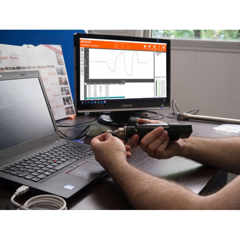 A hand reaching for a torque wrench on a cluttered workbench, with various electronic devices and cables scattered around